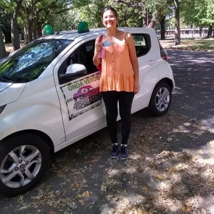 Alumna de Onda Verde con su licencia de conducir recién obtenida, al lado del auto de la escuela